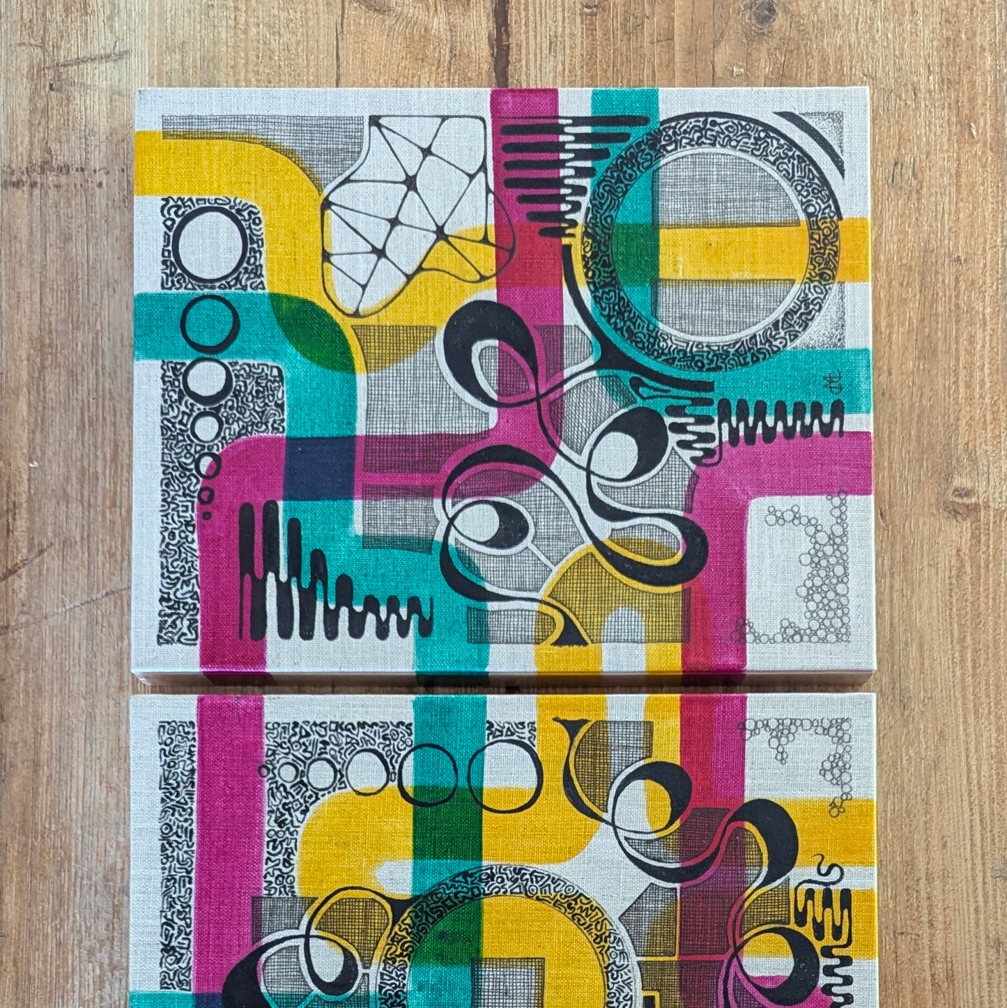 Two geometric artwork patterned on boards on a wooden surface
