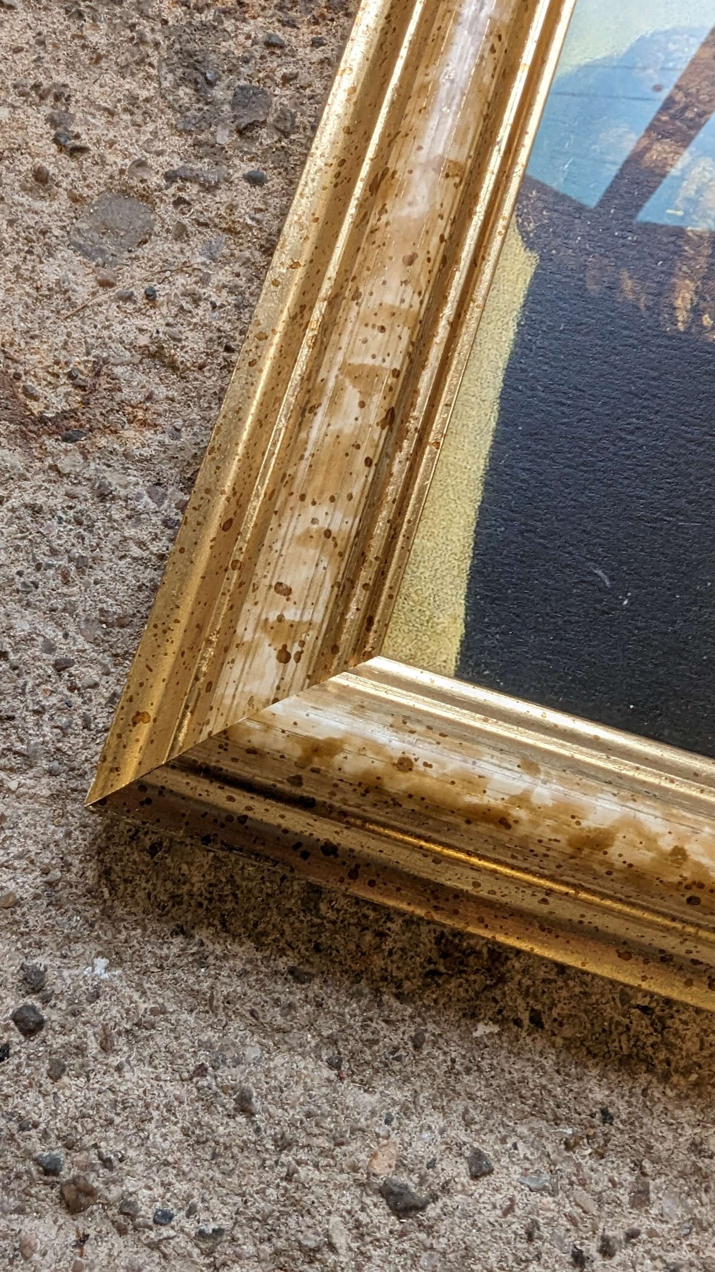 Gold-framed painting leaning against a textured wall.