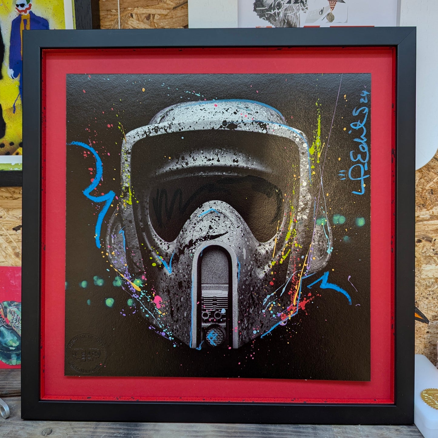 lp edits tree hugger float mounted on red card, frame is smooth black with red slips that have been splattered with pink blue purple paint, artwork is resting on wood shelf