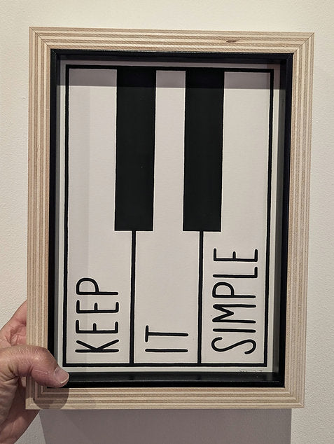 mr bingo keep it simple text on piano style black and white print, framed in plywood frame with black slip, entire frame and artwork is shown