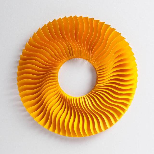 close up of round paper sculpture creating a wave effect in a circle with a hole in the middle. paper is yellow in colour against white
