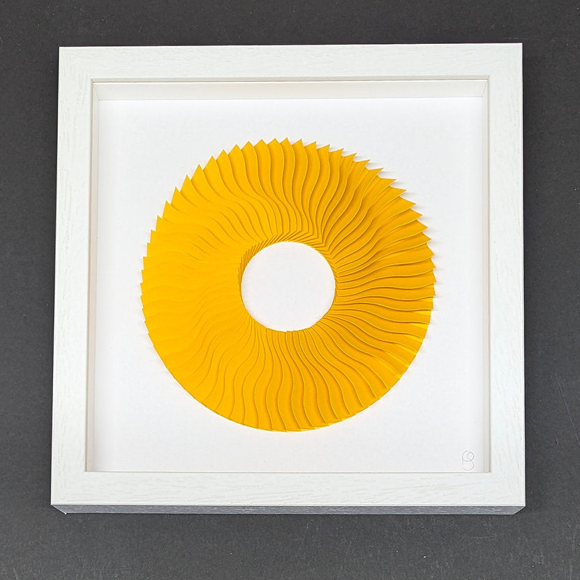 white box frame on black backgroud artwork is a paper sculpture creating a wave effect in a circle with a hole in the middle. sculpted paper is yellow in colour against white,