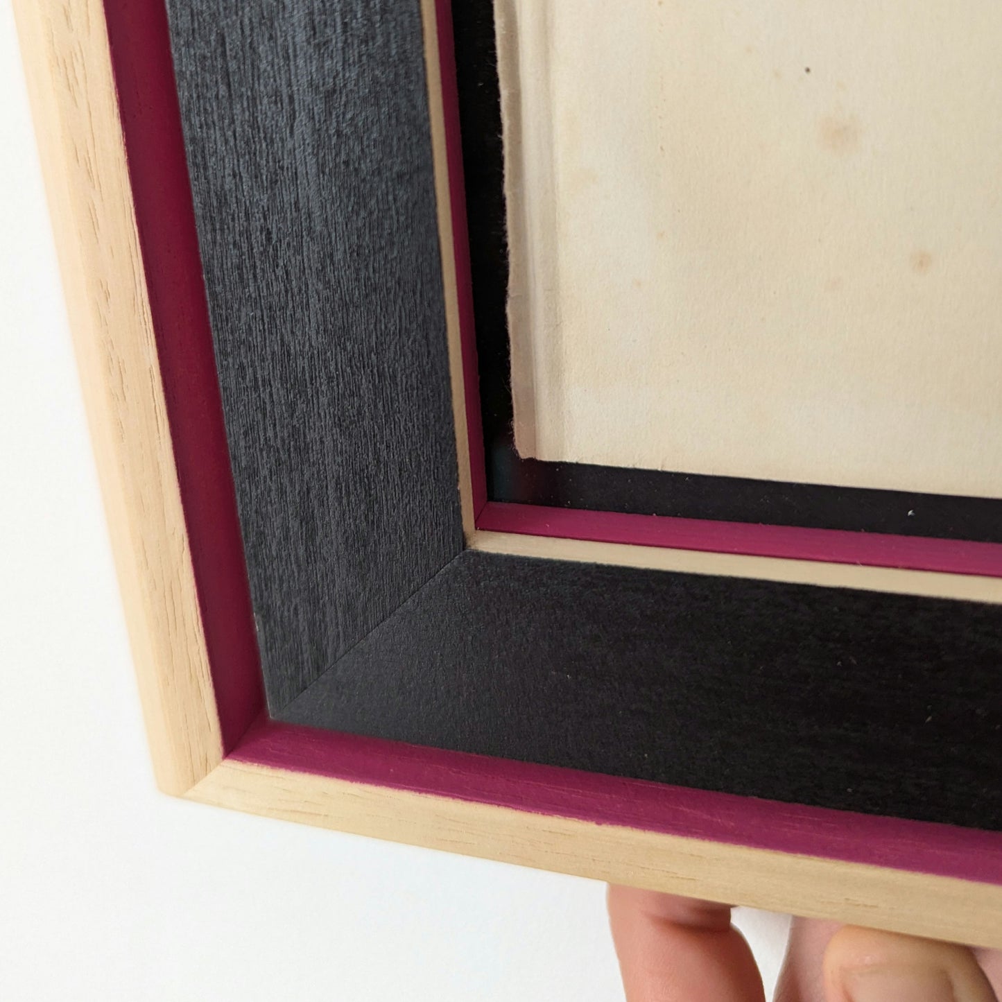 close up details of a picture frame, frame is made up of two mouldings, outer frame is natural wood that has pink details and internal frame is natural wood with black and pink details