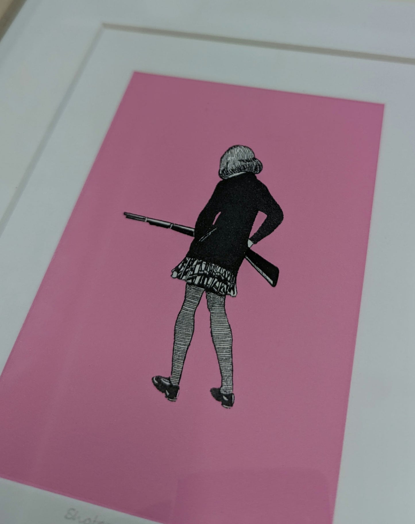 close up of mount and artwork CEAL WARNANTS 'SHOTGUN CLARE' Ltd Ed, artwork is of a girl with back to us holding a rifle, the styel is 1940s sketch on vivid pink background.