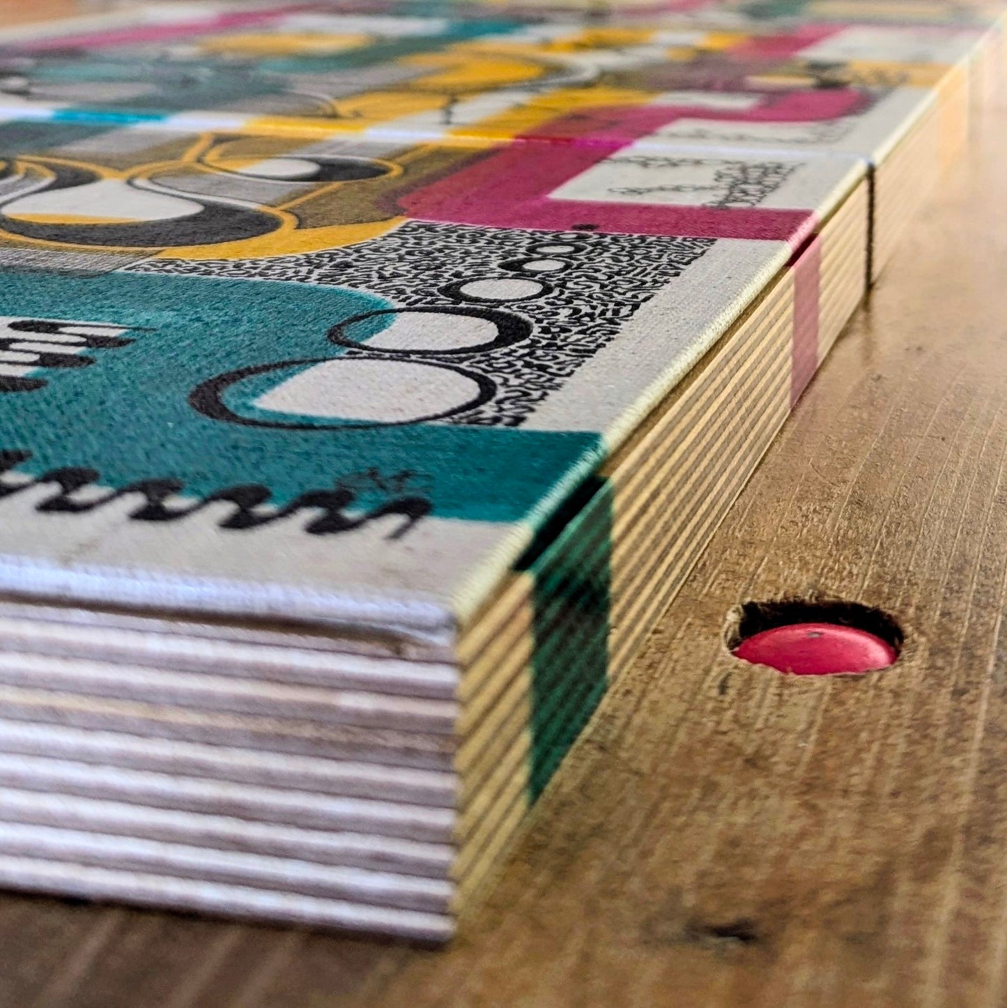 Colourful artwork with geometric patterns drawn on board mounted to plywood placed on a wooden surface