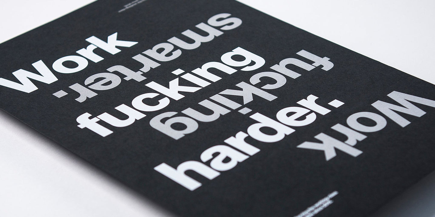 gfda poster on black paper with silver and white text, text states work fucking smarter, work fucking harder, close up of the text