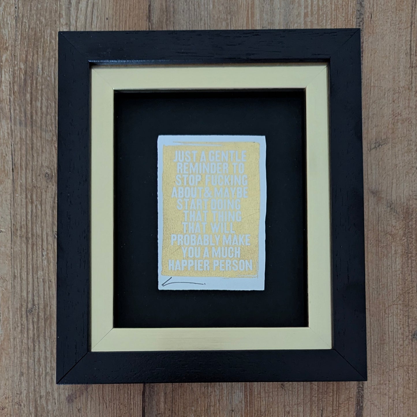 Framed Hackney Dave print with motivational quote printed with gold leaf on a wooden surface