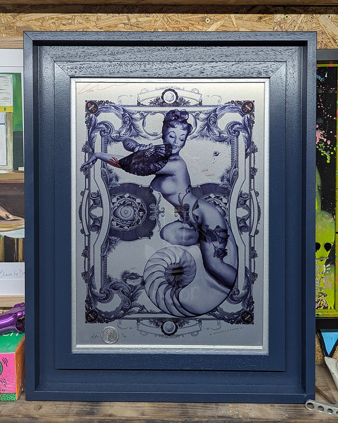 handiedan artwork on a silver aluminum sheet, tattoo style naked woman laying over flowers, artwork is in a double frame, a small inner silver frame and a st ives style frame in blue