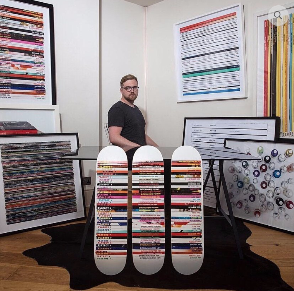 picture of mark vessey sat in room with selction of his artwork including a triptych of his playboy skateboards