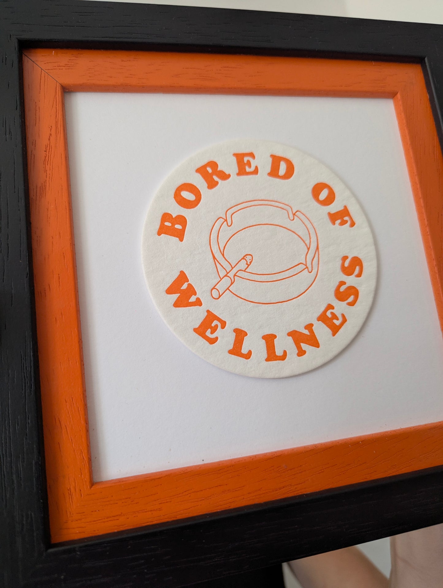 Round sign with 'Bored of Wellness' text in an orange circle, framed in black and orange.