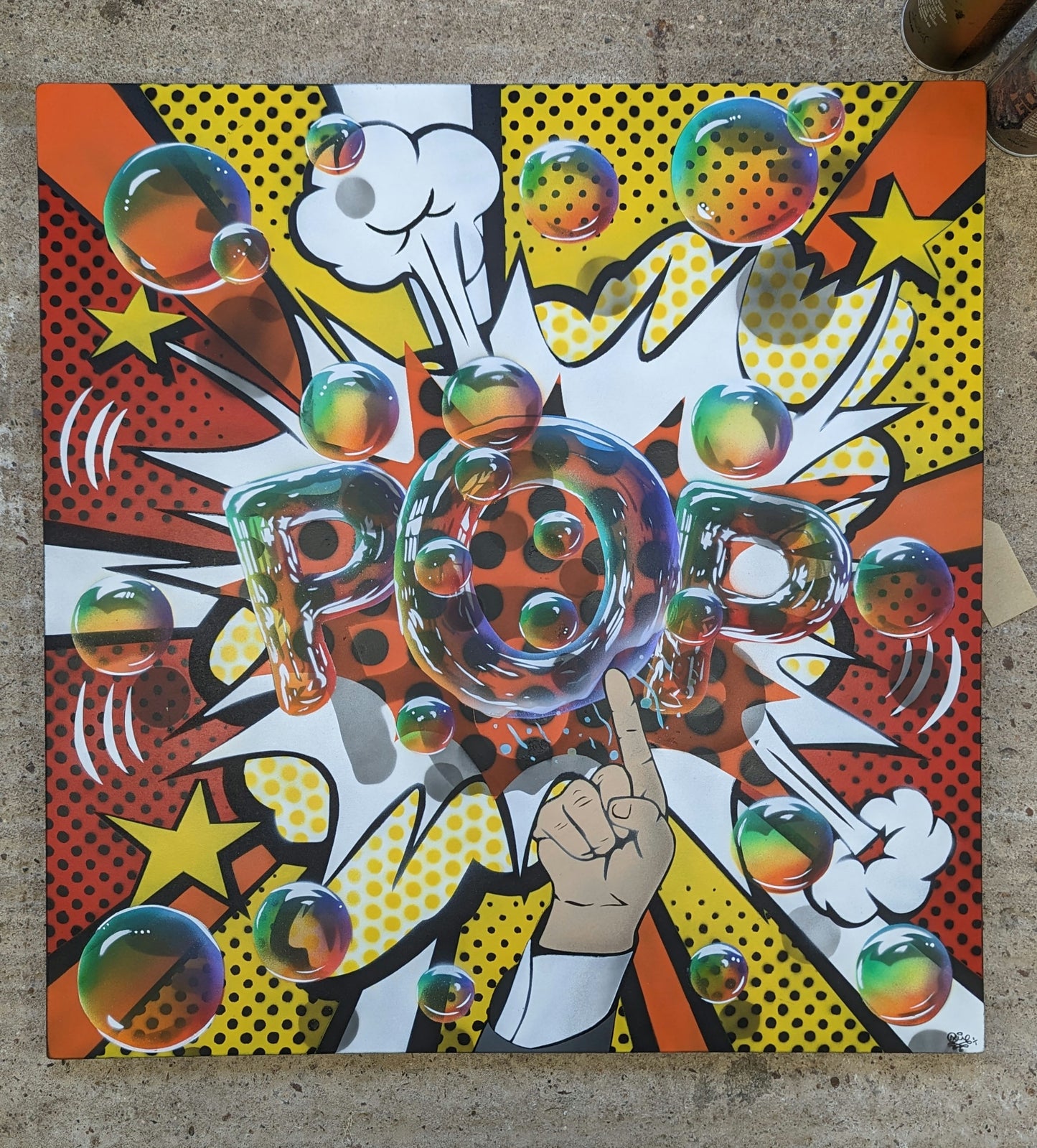 Colourful artwork with a hand pointing to a 'POP' bubble, inspired by Roy Lichtenstein style, on concrete background