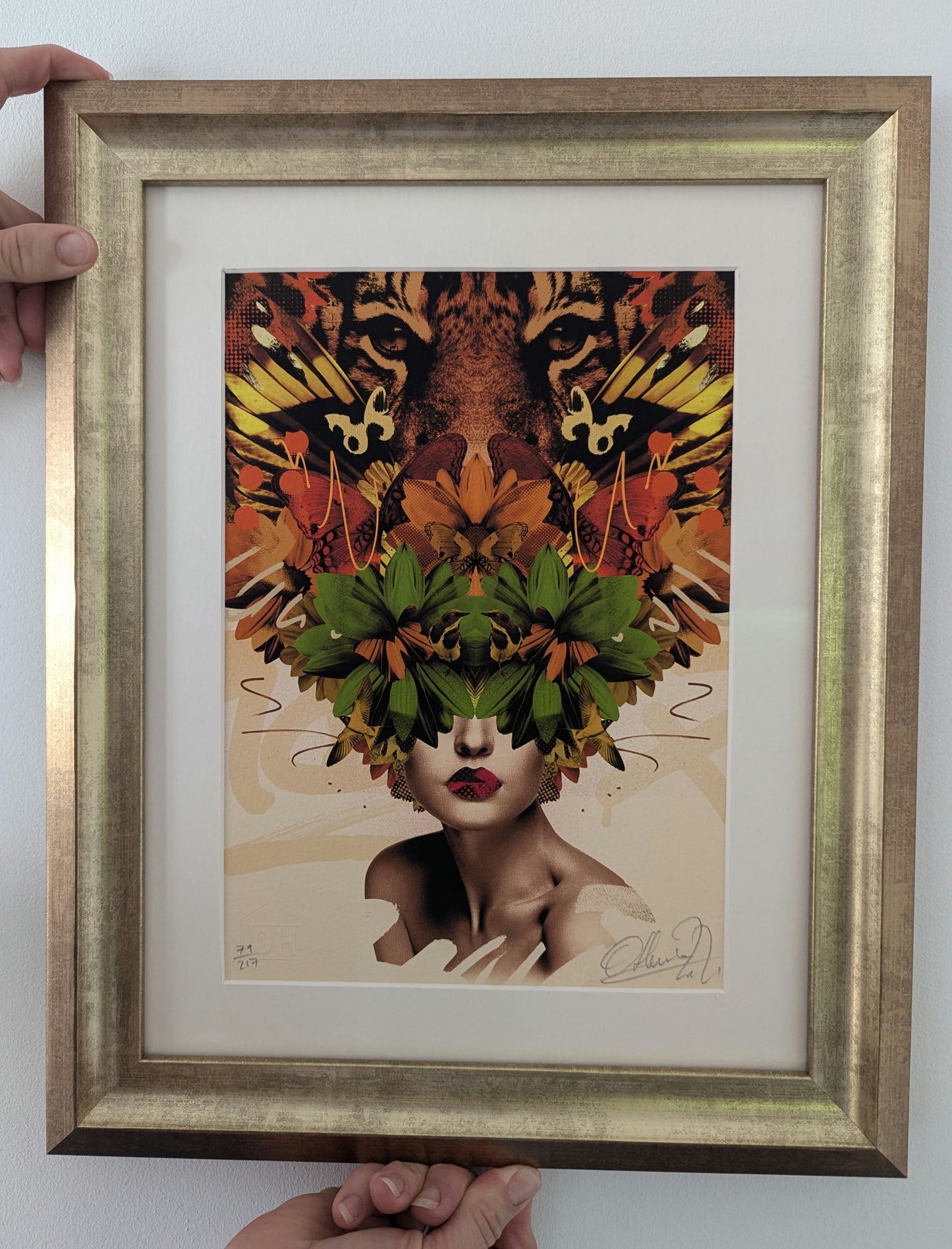 olly howe artwork on gold frame, the artwork is a collage style a womans face but her eyes and head are leaves and a tiger face, picture is being held.