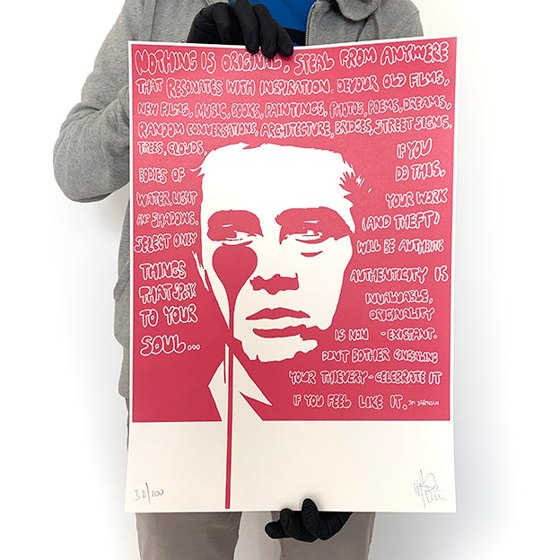 A person holding a limited edition Pure Evil James Dean print featuring a stylized, red-colored portrait with text.