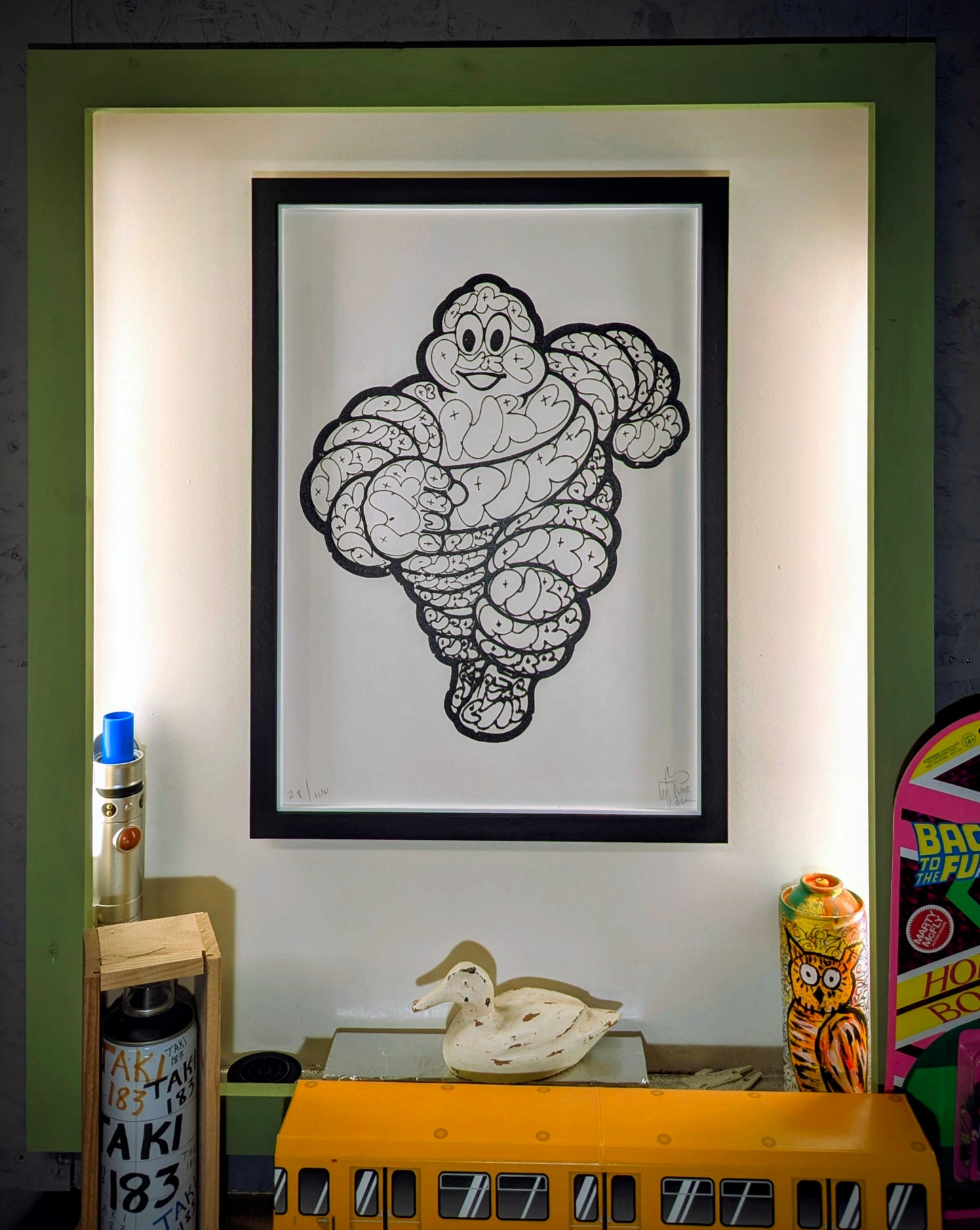 pure evil Michelin man full size in black frame, white slips. picture is on white wall with green surround.
