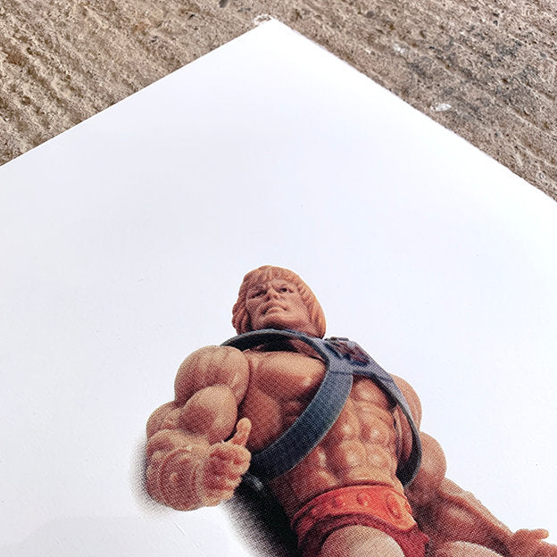 large print of he-man plastic toy, front of toy on show, image is the only colour on white paper. paper is on concrete floor only showing corner of the image and top of he man