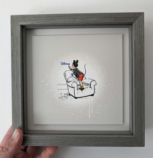 CHILD WITH MICKEY MOUSE EARS AND A TAIL STOOD ON A COMFY LOOKING ARMCHAIR, BLUE HAND PRINT ON CHAIR AND WRITING DISMAY IN DISNEY STYLE WRITING, IN A GREY PICTURE FRAME