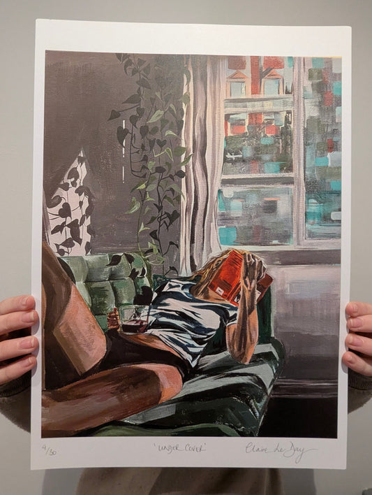 Art print of a living room and woman drinking a jug of wine scene held by two hands against a white background