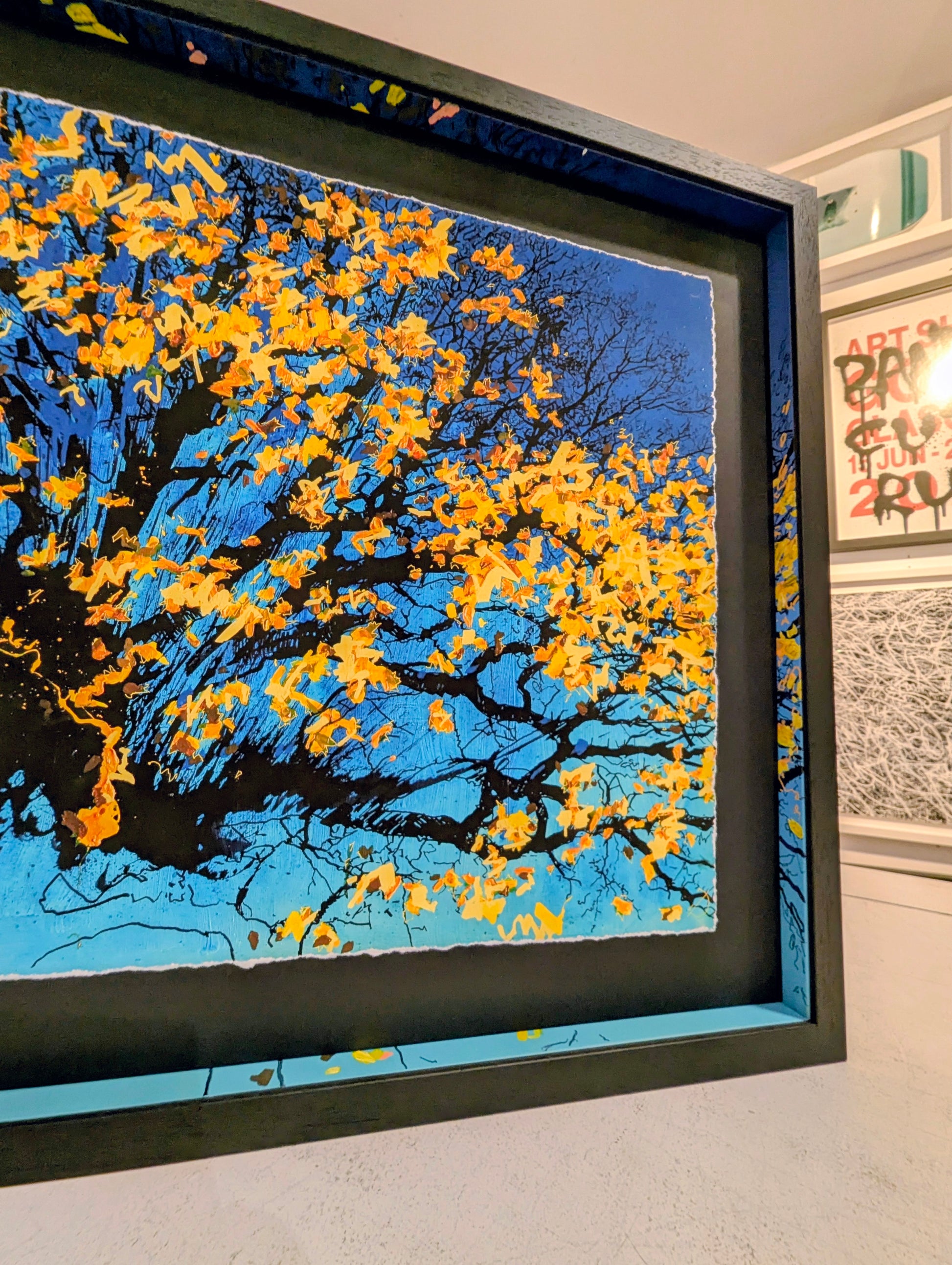 Corner of framed artwork of a tree with yellow leaves against a blue sky