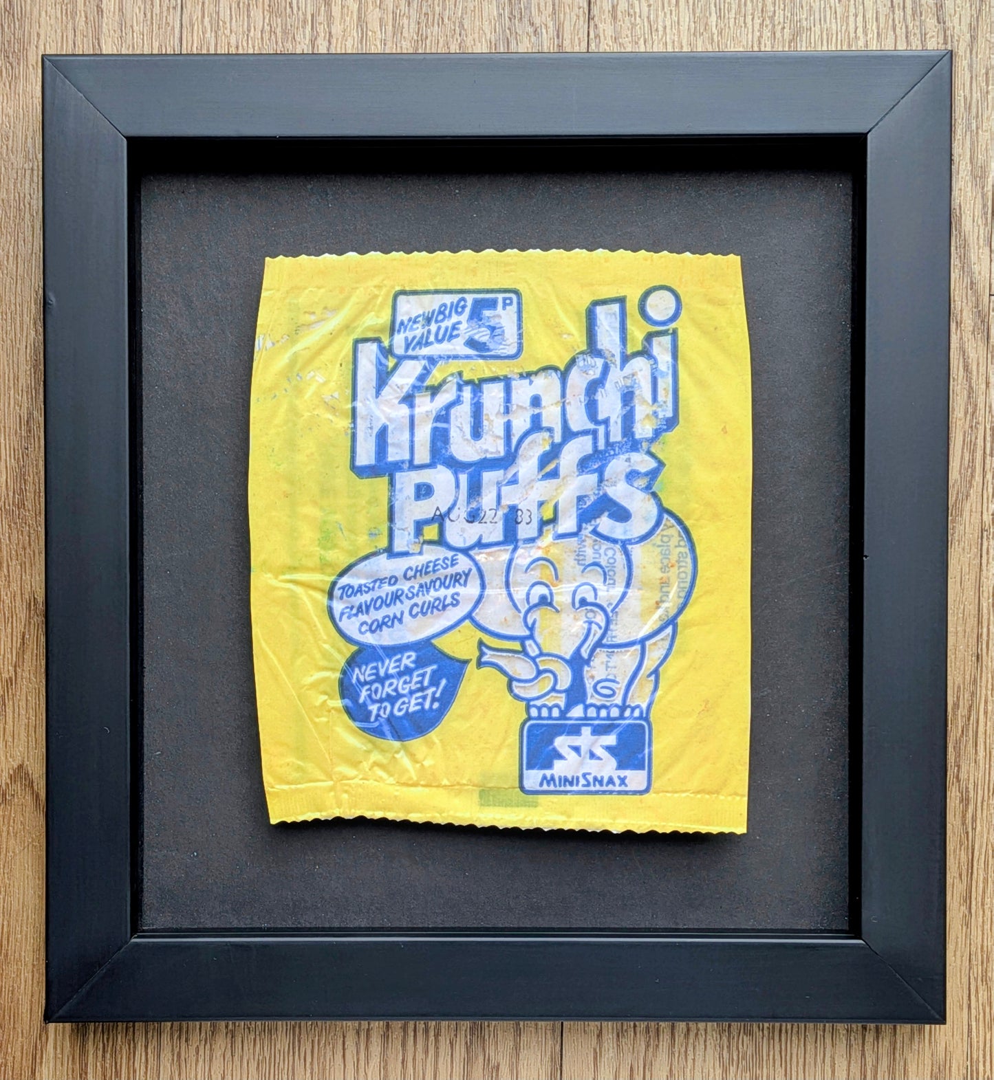 Framed yellow and blue Krunchi Puffs cereal package on a wooden surface