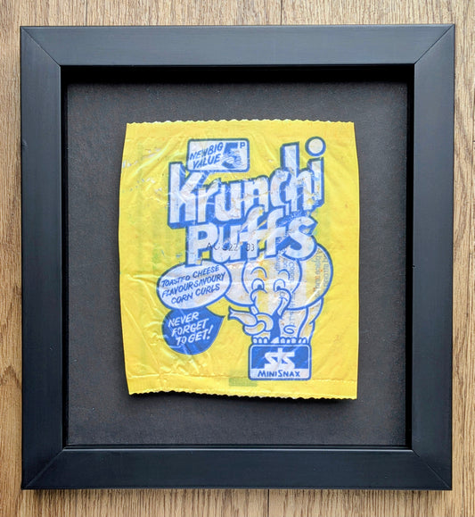 Framed yellow and blue Krunchi Puffs cereal package on a wooden surface