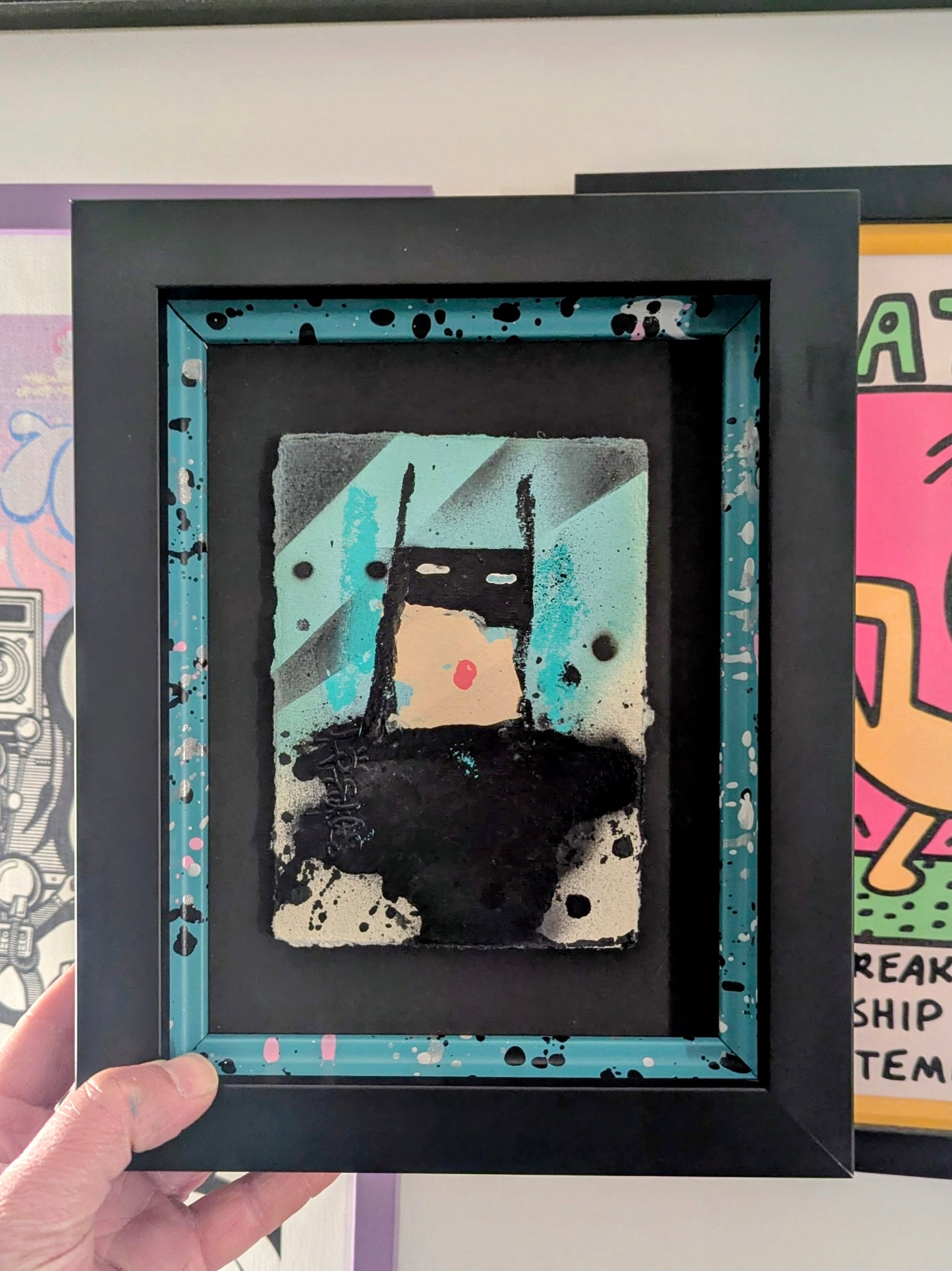 mini cartoon batman in black frame with colourful slips, artwork in background