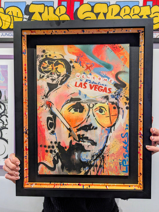 Framed artwork with a colorful portrait and text 'Welcome to Fabulous Las Vegas' held by a person.