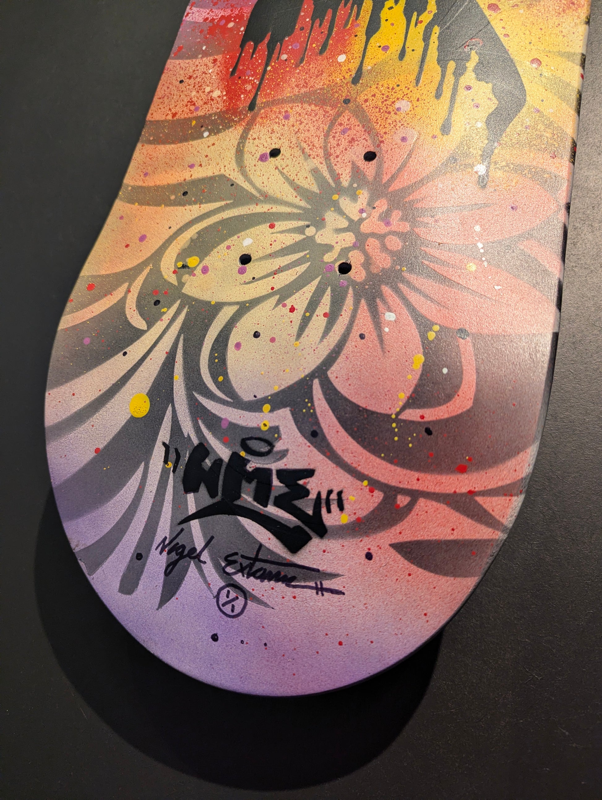 bottom of multicoloured skateboard with nme signature on black background