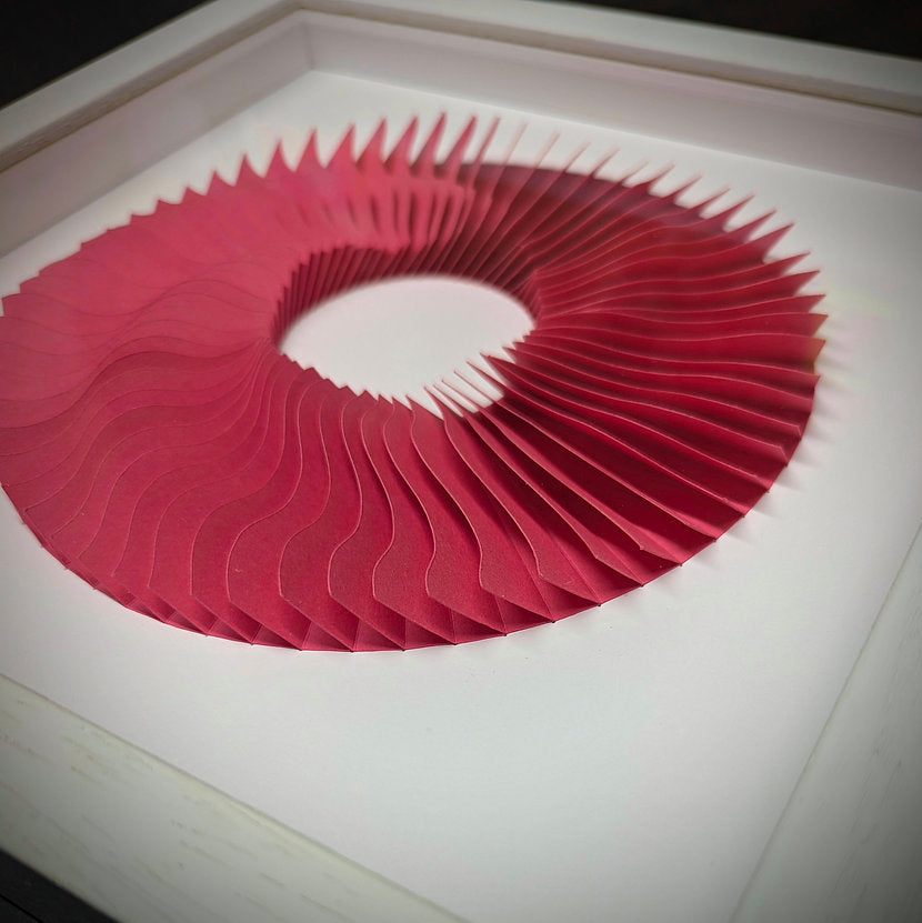 Paul Spencer paper sculpture. its round shaped with a clear middle, the pink paper is layered to create a wave effect, close up of the pink paper and the white box frame.