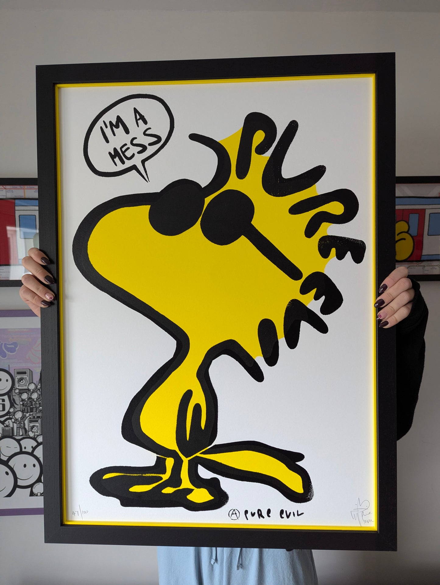 Framed artwork of a yellow cartoon character with text holding a framed picture.