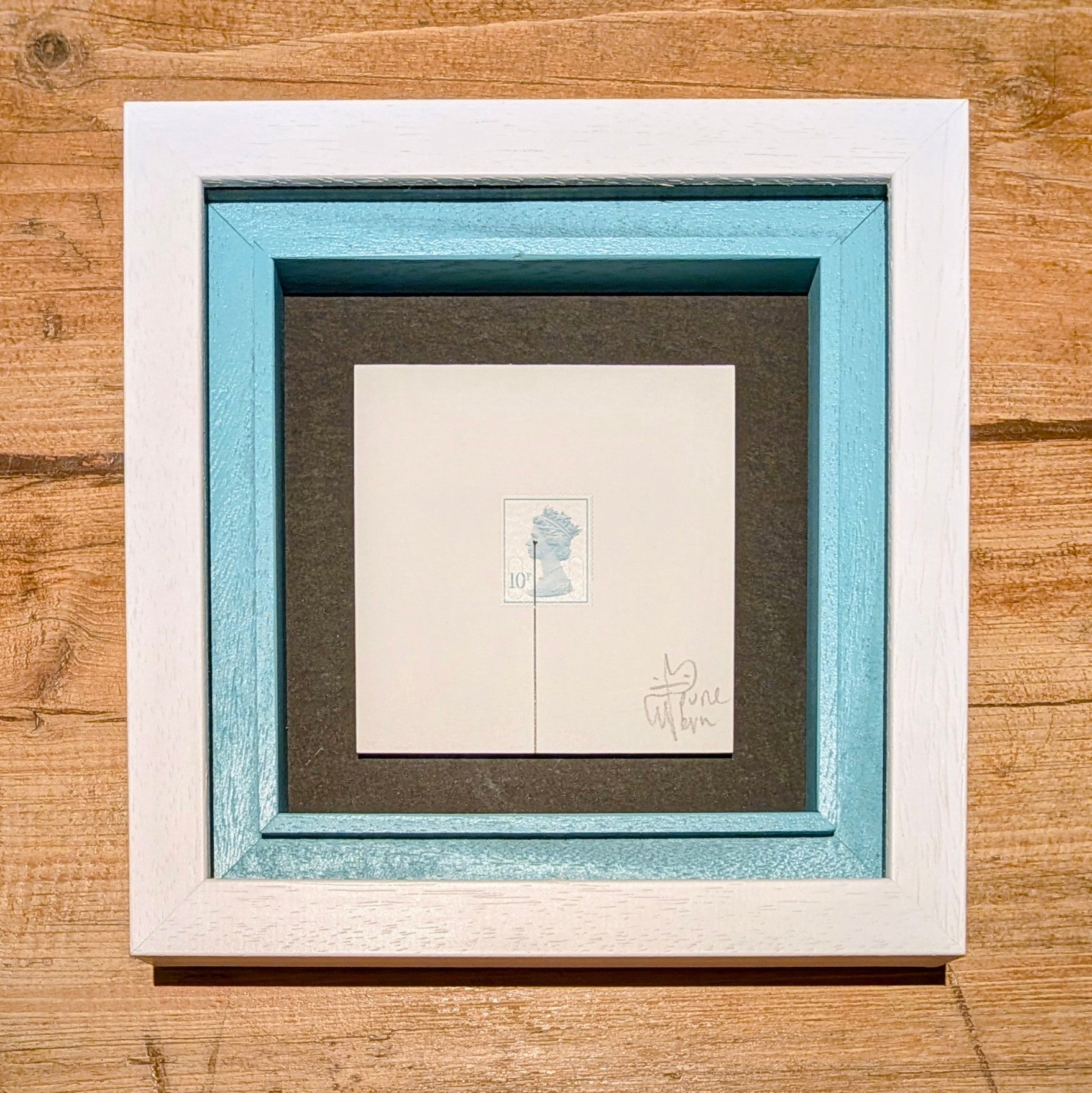 Framed artwork with a white border and blue inner frame on a wooden surface
