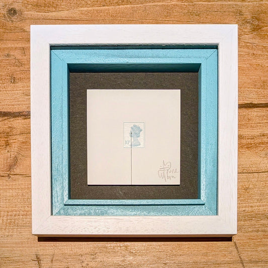 Framed artwork with a white border and blue inner frame on a wooden surface