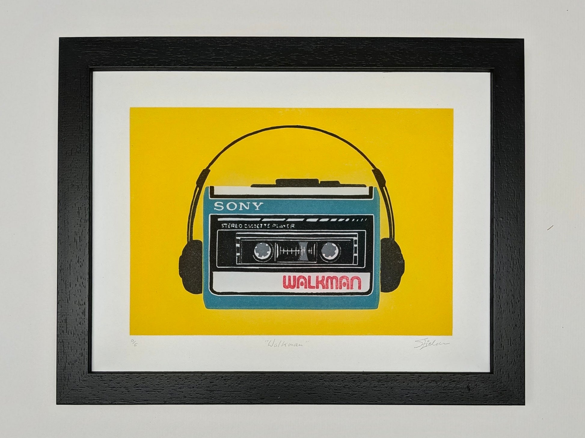 A framed art print featuring a retro Sony Walkman cassette player with headphones on a bright yellow background, enclosed in a black frame with a white mat.