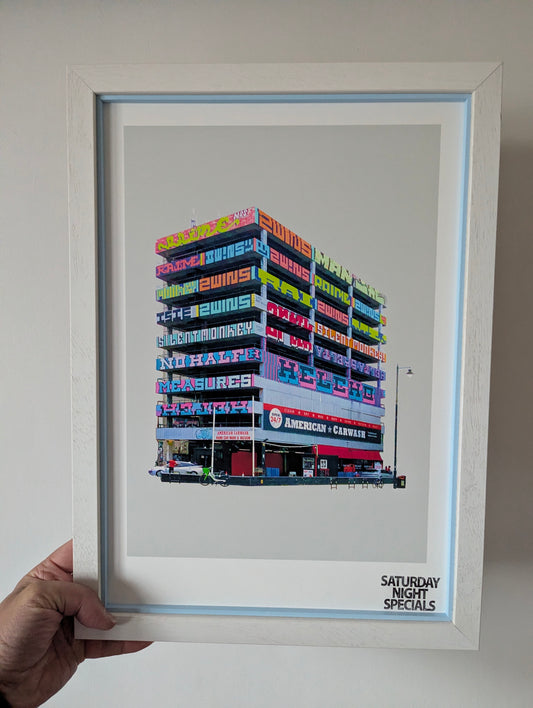 Framed artwork of a colourful graffiti building with 'Saturday Night Specials' text. hand holding against white