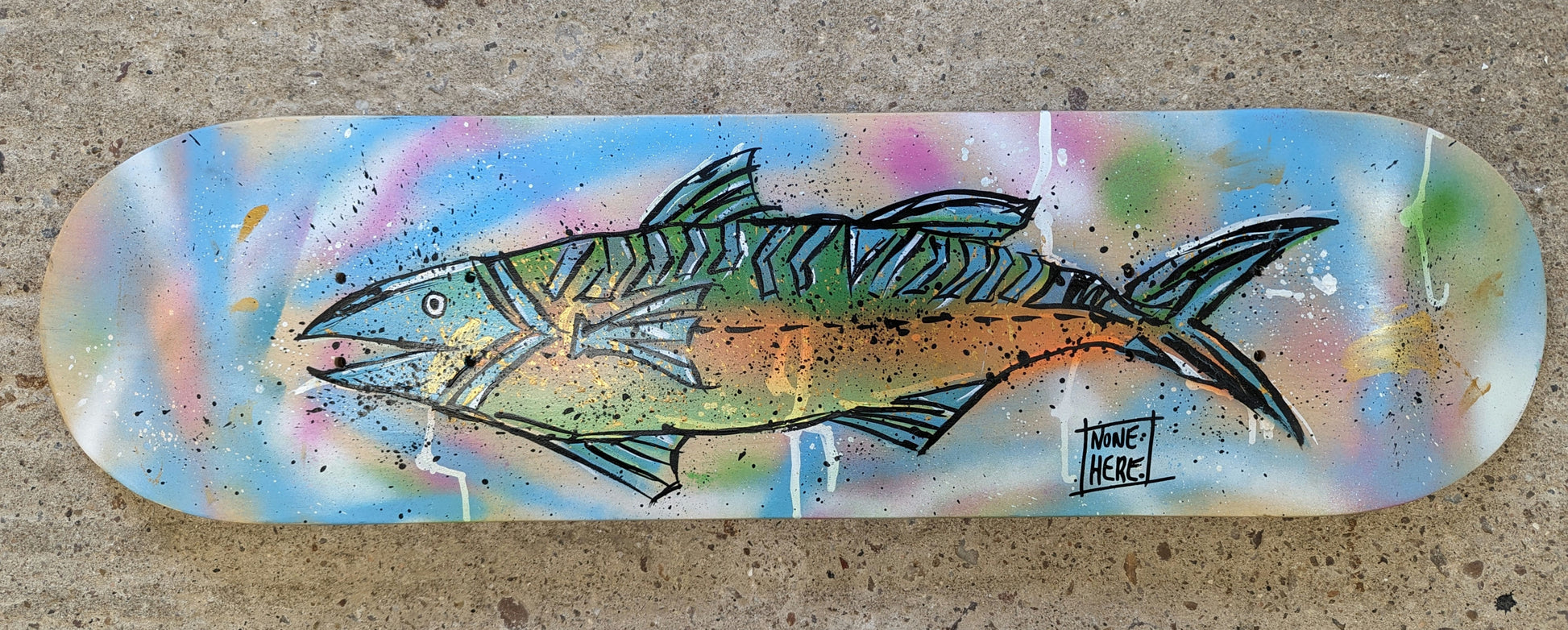 Steve McCracken painted skateboard, freehand style colourful fish with greens and blue fins painted on a background of blue and pink spray and splatter. skateboard is resting on a concrete floor.