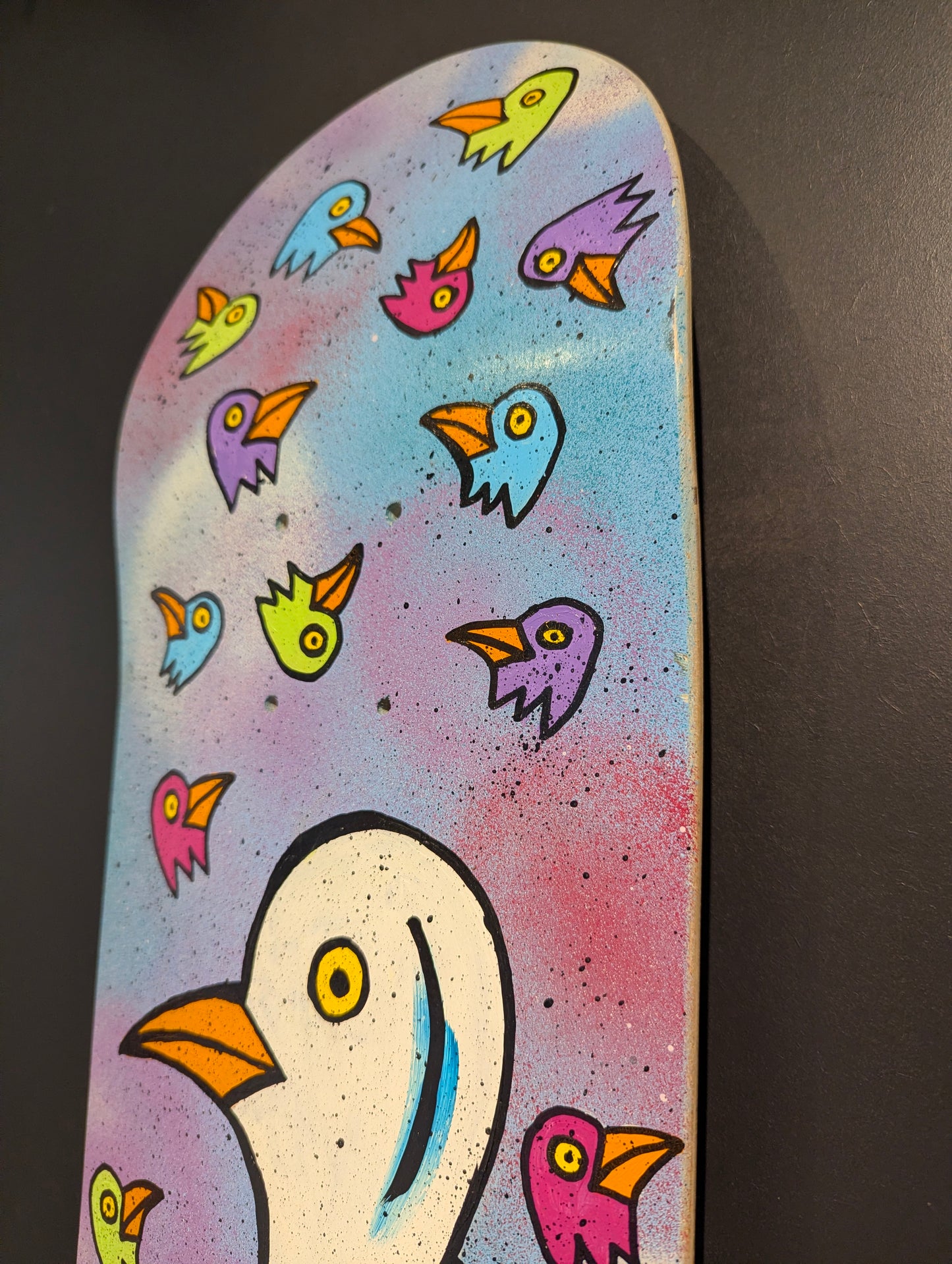 Skateboard deck with colorful bird illustrations on a dark background