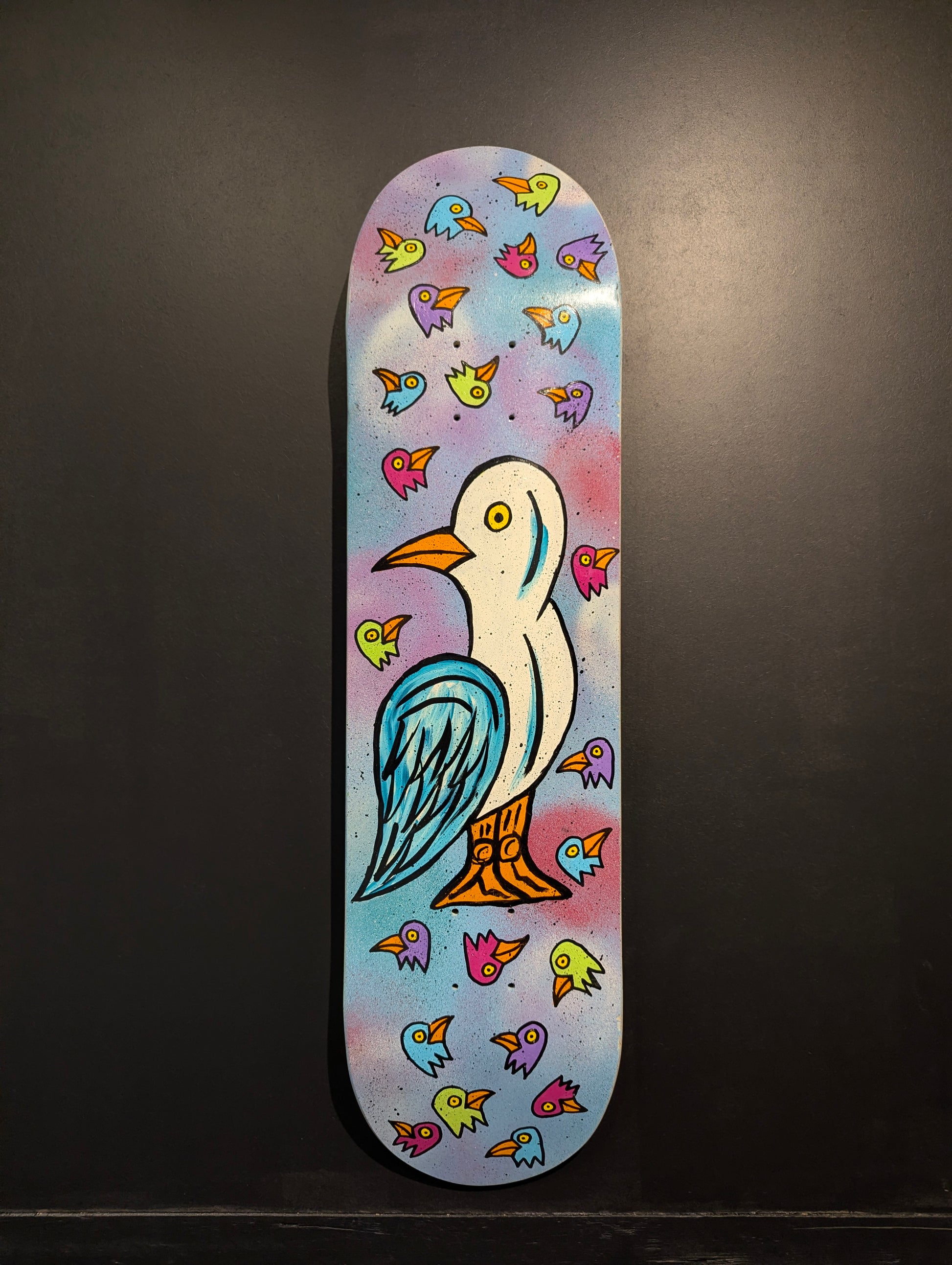 Skateboard deck with a colorful bird design on a dark background
