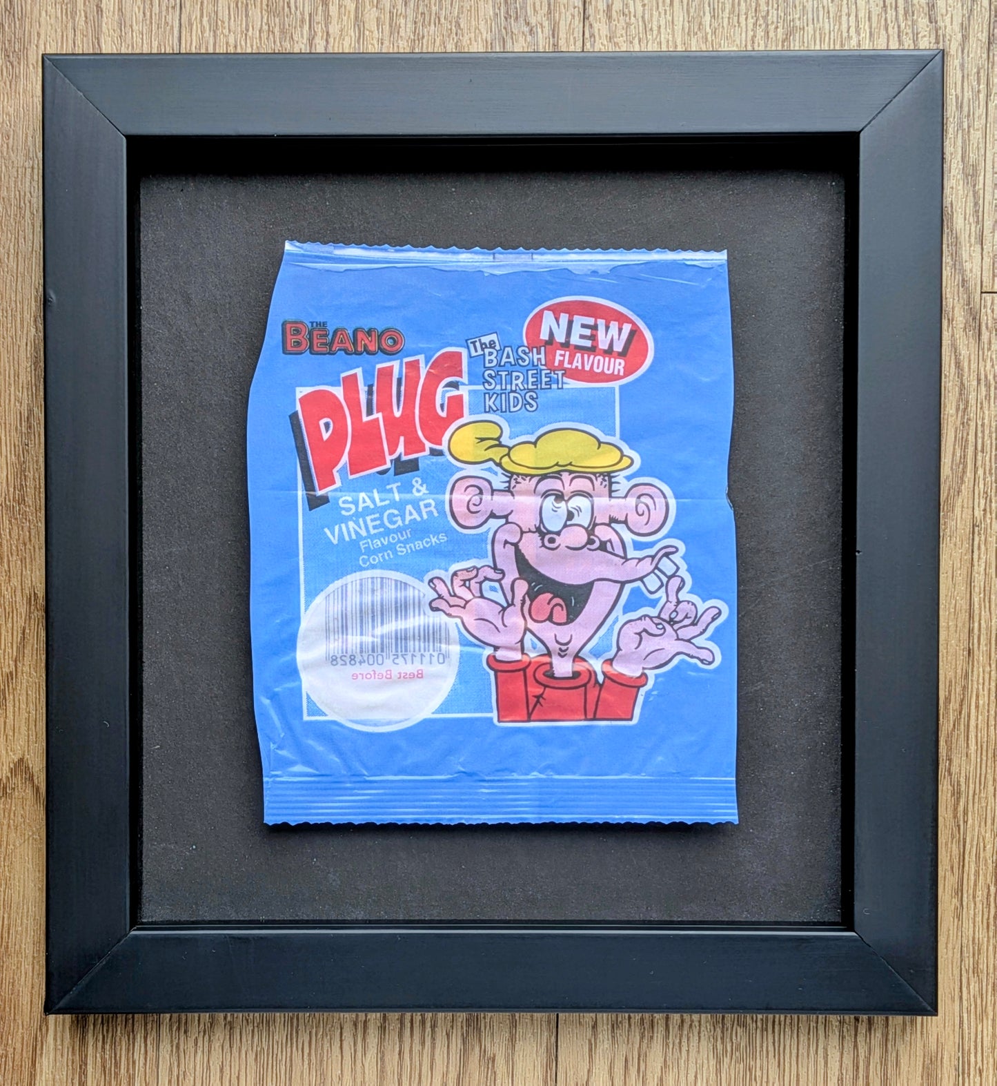 Framed blue packet of Beano Plug Salt & Vinegar crisps on a wooden surface