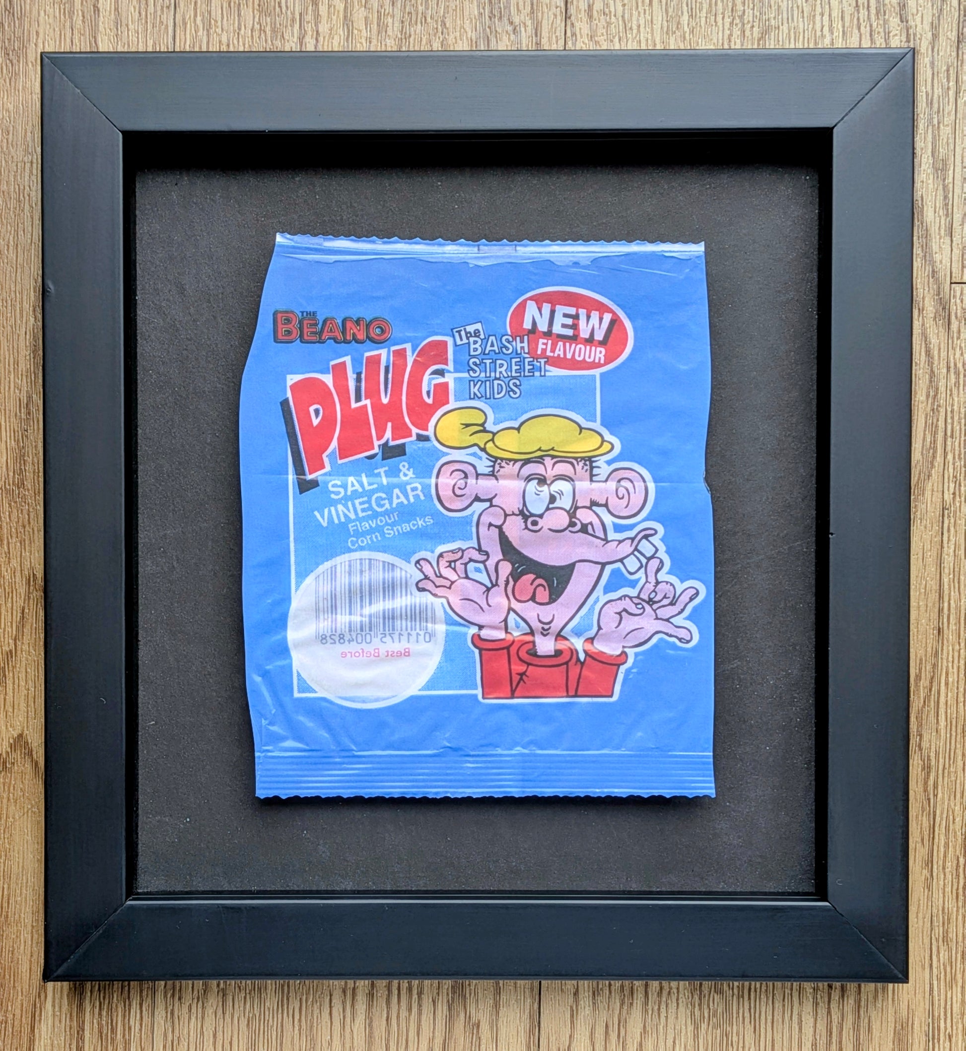 Framed blue packet of Beano Plug Salt & Vinegar crisps on a wooden surface