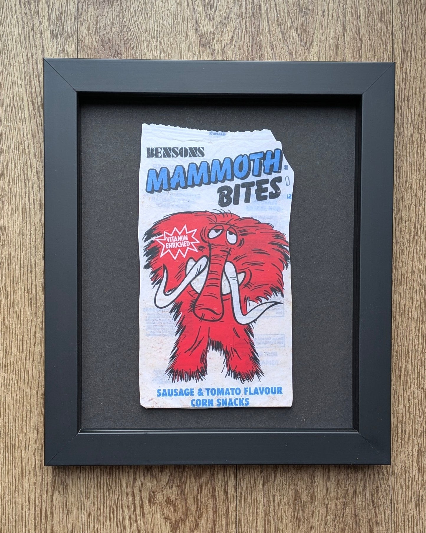 Framed artwork of a vintage-style snack packet design on a wooden surface