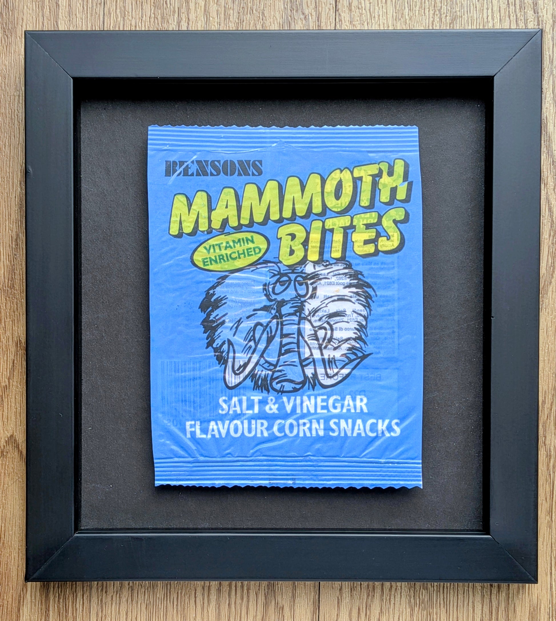 Framed packet of Pensons Mammoth Bites salt and vinegar flavor corn snacks on a wooden surface.