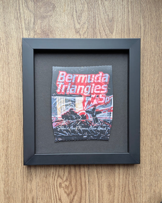 Framed crisp packet artwork with 'Bermuda Triangles' text on a wooden surface