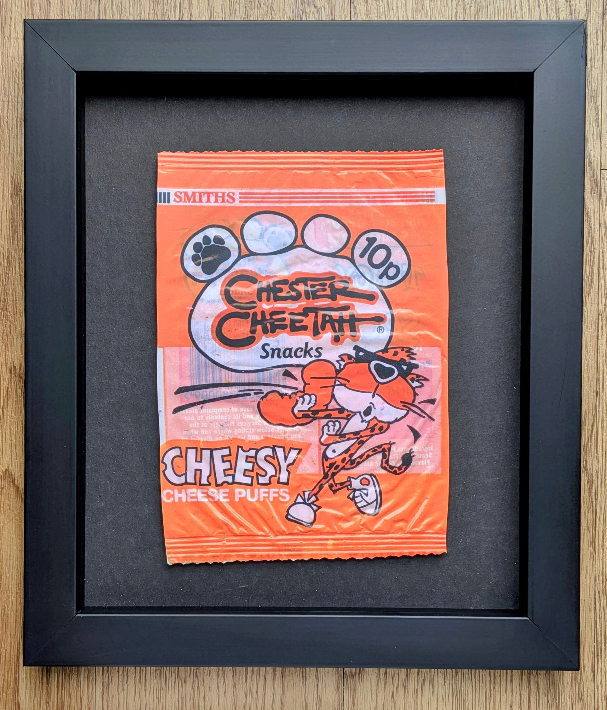 Framed vintage-style Cheetos snack packet on a wooden surface