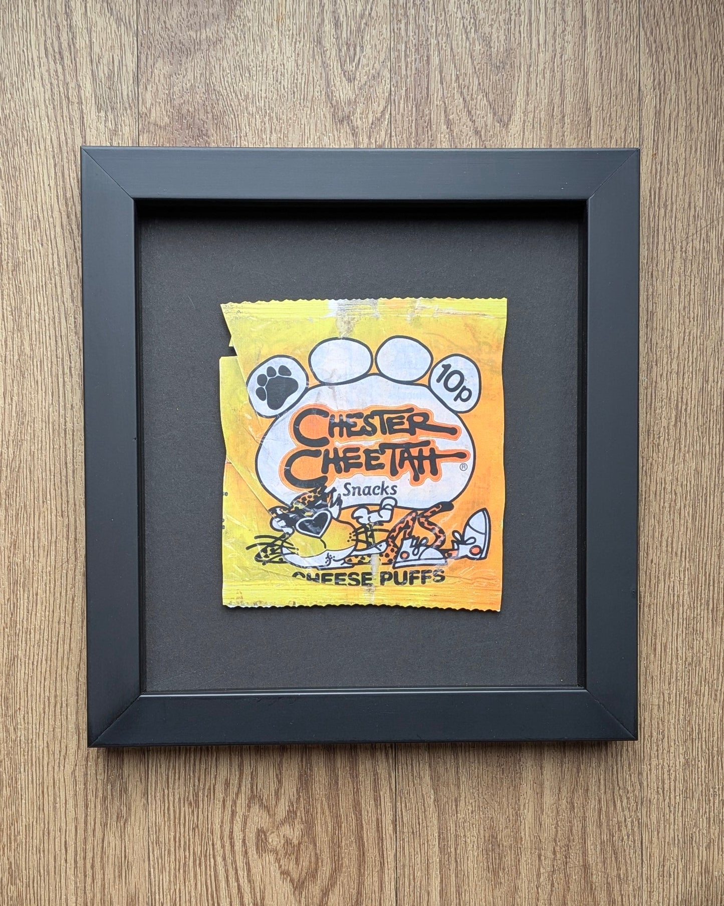Framed Chester Cheetah snack packet on a wooden surface