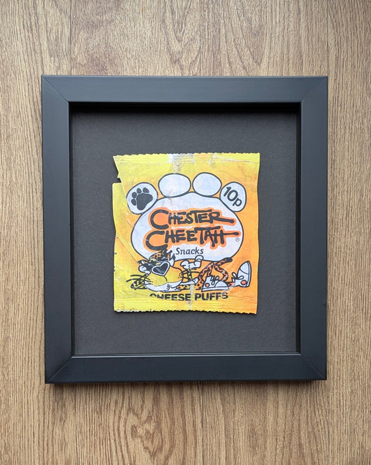 Framed Chester Cheetah snack packet on a wooden surface