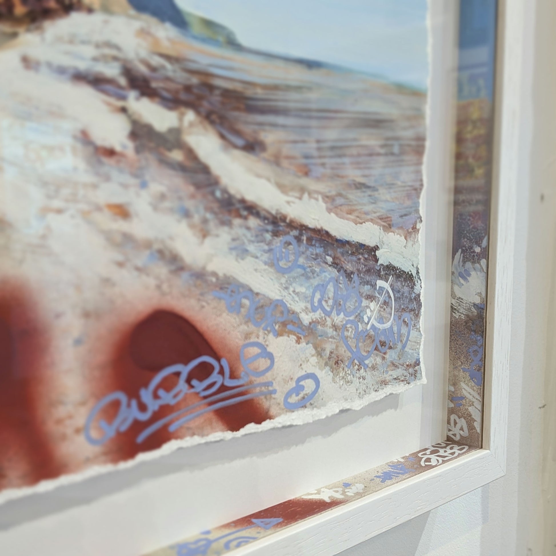 close up of white frame,the slips in the frame are colour matched to the artwork, artwork is if the sea and cliffs .
