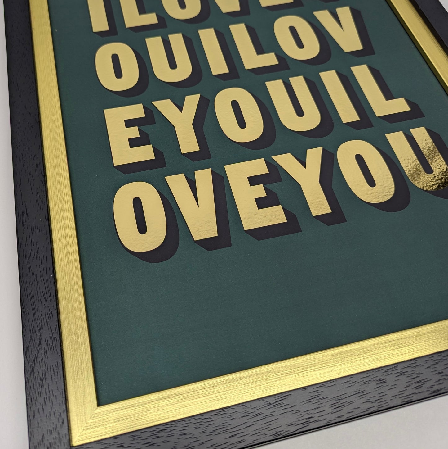 Framed painted by amy artwork with gold i love you text on a green background, corner close up shot of gold inner frame and black frame
