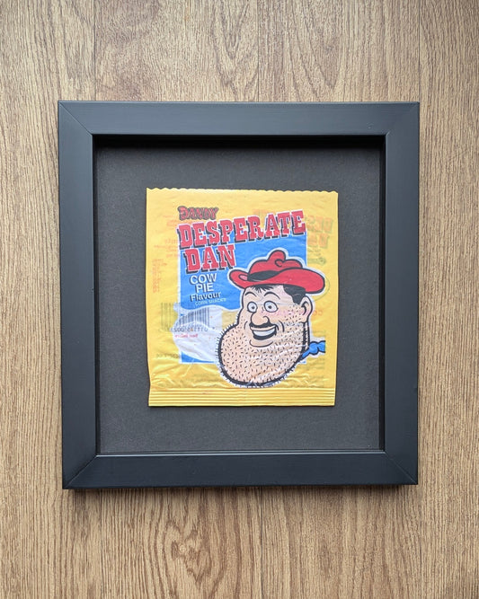 Framed Desperate Dan candy wrapper on a wooden surface