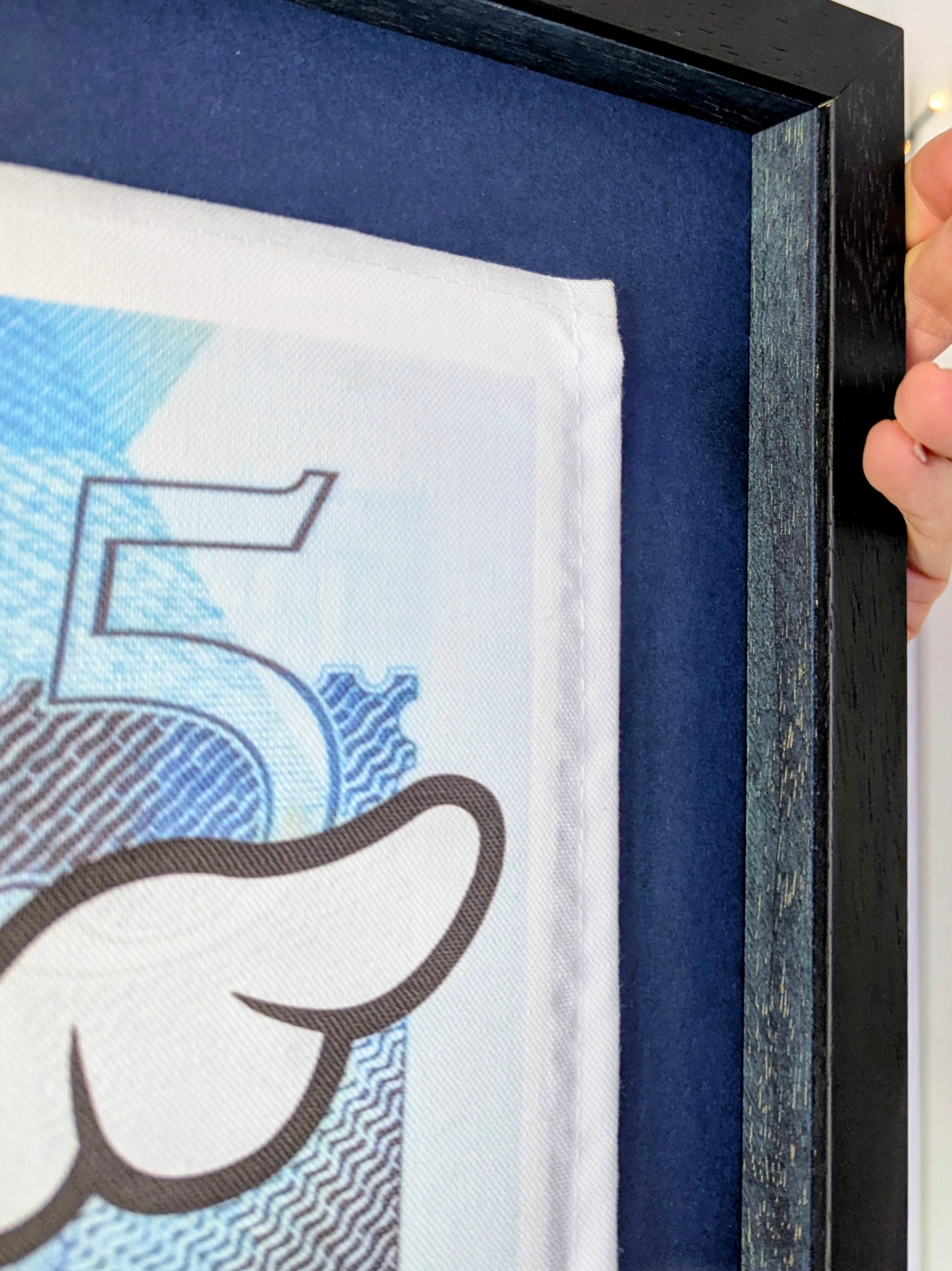 Close-up of a hand holding a black-framed artwork with a blue background