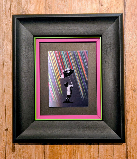 boy holding umbrella with colourful rain in black frame with colourful slips, against a wood background