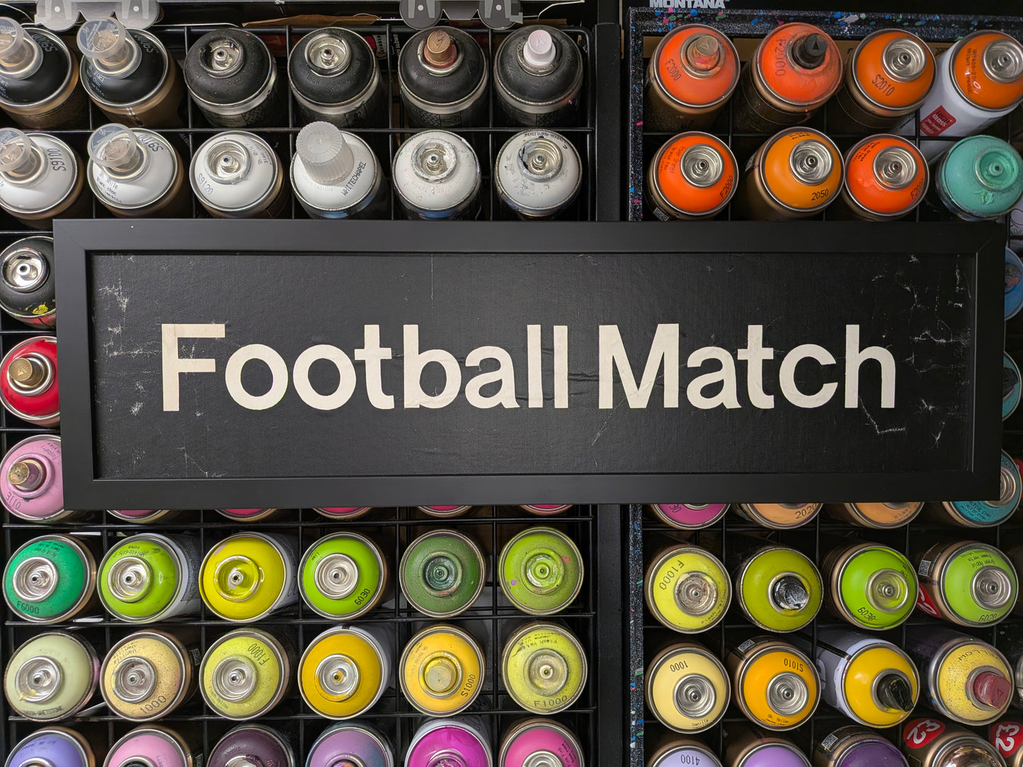 Colorful spray paint cans with a sign reading 'Football Match' on a black background.